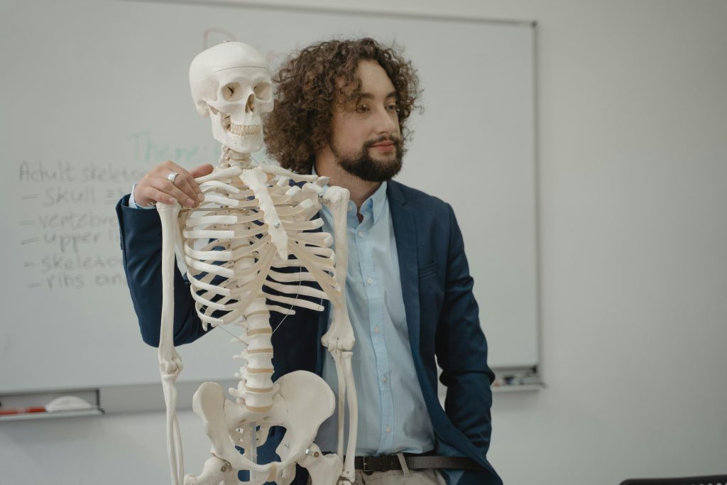 Educator demonstrating human skeleton model during a biology lesson in a school classroom.